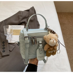 Detail der hellblauen gewebten Zylindertasche mit Teddybär-Anhänger und silberner Kette