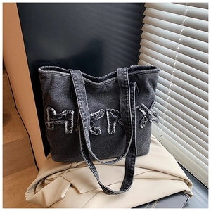 Detail of washed black denim tote bag with raw-edge MK letter patch and sturdy dual handles