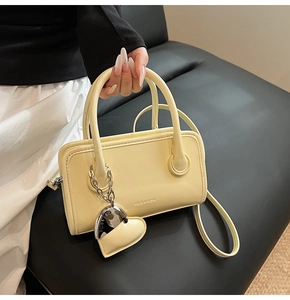 Detailed view of cream yellow leather handbag with heart charm and engraved logo
