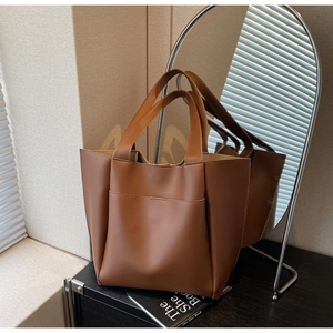 Detailed view of a brown leather tote bag with a front pocket on a black wooden surface