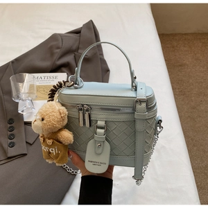 Detail der hellblauen PU-Handtasche mit Webstruktur und einem süßen Bären-Anhänger