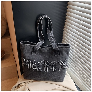 Close-up of distressed denim tote bag featuring frayed letter patches and washed texture