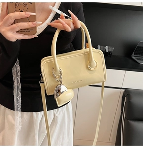 Detail of a creamy yellow matte leather handbag with CLEAЯOK logo and heart charm