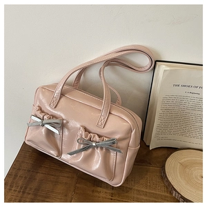 Close-up of pink shoulder bag with ruffle pockets and silver bow details on wood surface