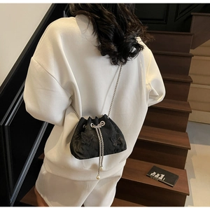 Detail of black drawstring bucket bag with butterfly patches and pearl accents