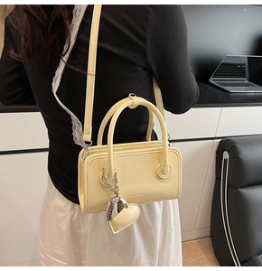 Creamy yellow Boston bag with heart charm and adjustable strap shown on shoulder