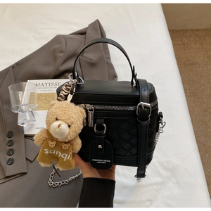 Detail einer schwarzen gewebten Box-Tasche mit Silberkette und kleinem Bären-Anhänger