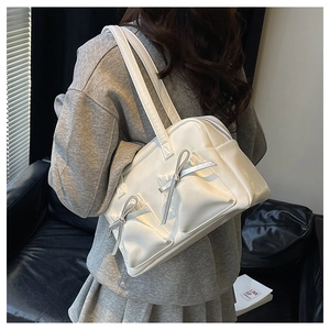 Detail of white glossy leather shoulder bag featuring decorative front bow pockets