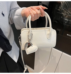 Detail view of a white leather handbag featuring heart-shaped charm and logo texture