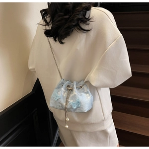 Detail of light blue lace bucket bag with floral patterns, chain strap and pearl drawstring