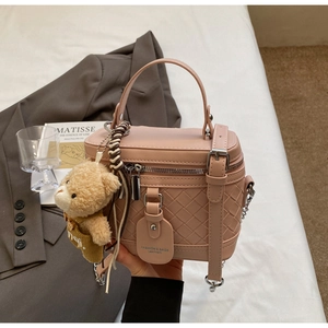 Detailansicht einer rosa Box-Tasche mit Webstruktur und süßem Bärenanhänger-Dekor