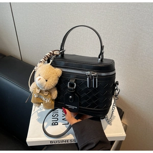 Detail einer schwarzen gewebten Box-Tasche mit Metallreißverschlüssen und süßem Bärenanhänger