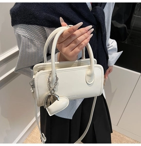 Detail of off-white crossbody bag with silver heart charm and metal chain strap