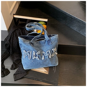 Close-up of denim tote bag with textured MKMK lettering on a vintage staircase