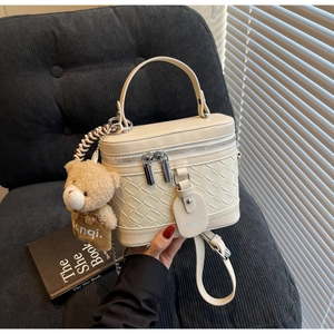 Detailansicht der cremefarbenen Box-Tasche mit Webstruktur und Plüschbär-Anhänger