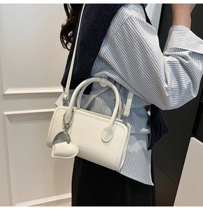 Close-up of white rectangular handbag with heart charm and leather texture detail
