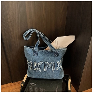 Detail view of denim tote bag featuring frayed edge letter patchwork and washed blue texture