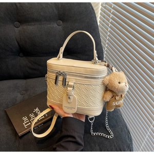 Detail der cremeweißen Box-Tasche mit Webstruktur, Rundgriff und süßem Teddybär-Anhänger