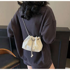 Detail of white bucket bag featuring floral textures, silver chain and pearl drawstrings