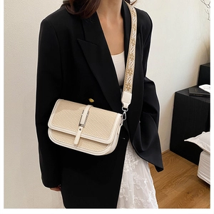 Detail of cream woven crossbody bag with decorative jacquard shoulder strap worn by model