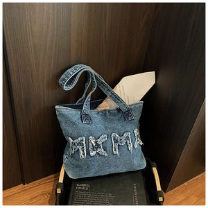 Detailed texture of washed denim tote bag featuring distressed MKMA letter applique