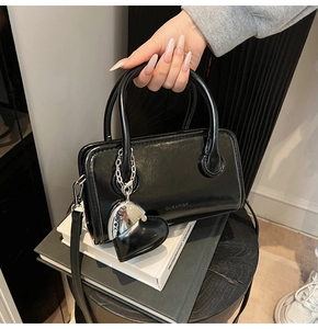 Detail of black glossy leather handbag featuring heart charm and detachable shoulder strap