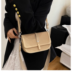 Detail of a beige woven crossbody flap bag with leather trim worn by a model