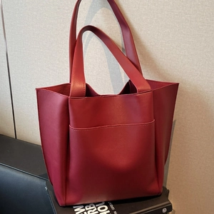 Minimalist red large capacity tote bag in matte leather on black book display