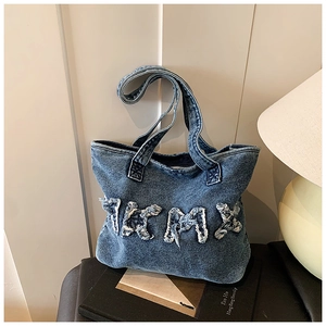 Detail of blue washed denim tote bag with white frayed TRMX letter embroidery on surface