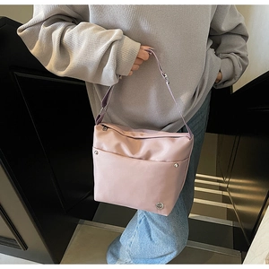 Gros plan d'un sac bandoulière rose en tissu oxford avec rivets et logo métallique