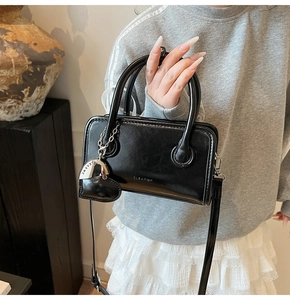 Detail of a minimalist black waxed leather handbag with silver logo and heart charm