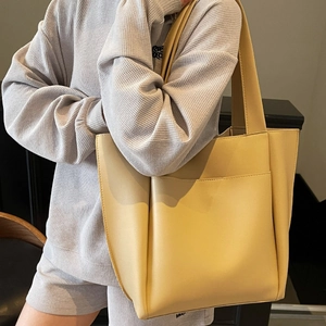 Minimalist beige tote bag with wide strap and front pocket carried by a model