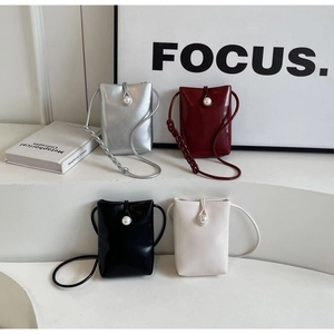 Detail of four colorful mini crossbody bags with large pearl clasps on white pedestals