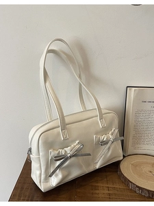 Creamy white faux leather shoulder bag featuring silver bow charms and front pleated pockets