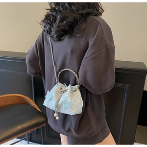 Detail of light blue embroidered bucket bag with floral patterns and pearl drawstring