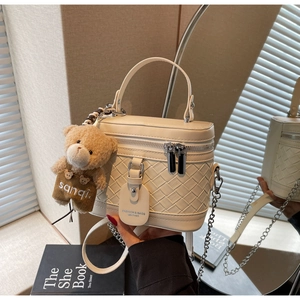 Detail der cremefarbenen Umhängetasche mit Flechtmuster und Teddybären-Anhänger
