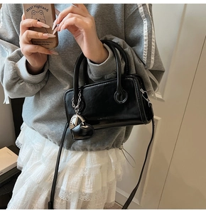 Detailed view of black leather mini square bag with heart pendant and silver charm