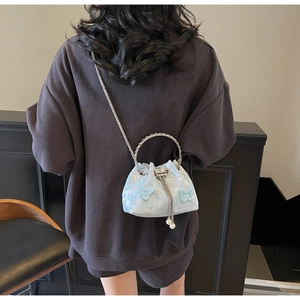 Detail of light blue bucket bag with butterfly embroidery, pearl charm, and chain strap