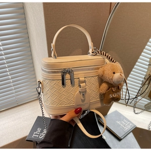 Detail der beige gewebten Box-Tasche mit Doppel-Reißverschluss und braunem Teddybär-Anhänger