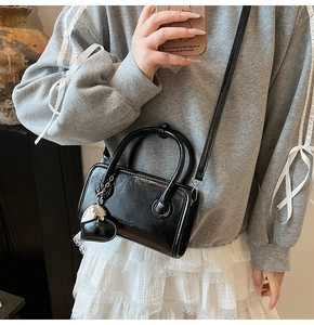 Detail of a black patent leather crossbody bag featuring heart pendant and dual handles