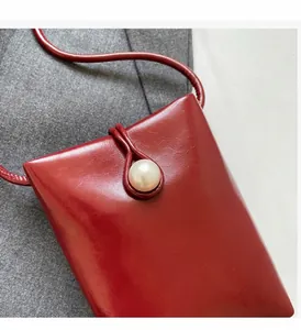 Close-up of bright red leather phone bag featuring a white pearl buckle and fine texture