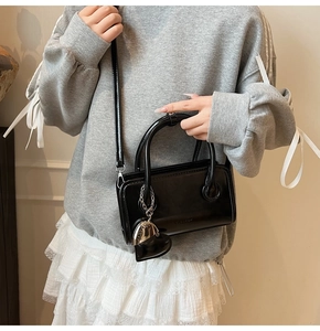 Detail of black glossy leather handbag with heart pendant and adjustable strap