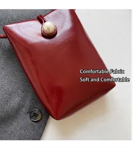 Detail of burgundy glossy leather phone bag featuring a large pearl clasp and strap