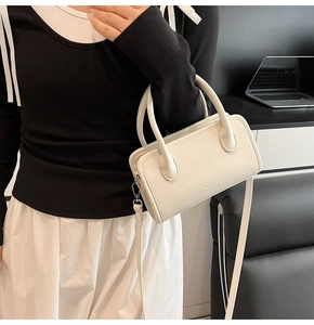 White minimalist leather crossbody bag shown being carried by a model in a modern interior