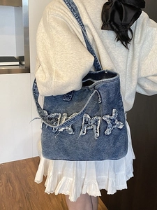 Retro washed denim tote bag with frayed KMX letters worn by a model in a modern room