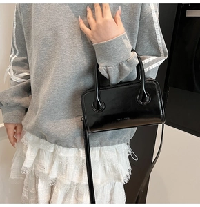 Detail of glossy black leather handbag with brand logo and adjustable shoulder strap