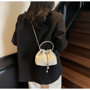 Detail of white drawstring bucket bag with floral embroidery and pearl tassel accent