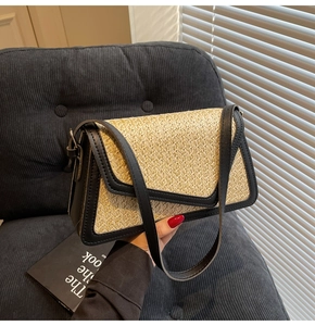 Detail of a straw crossbody bag with black leather trim resting on a dark velvet chair
