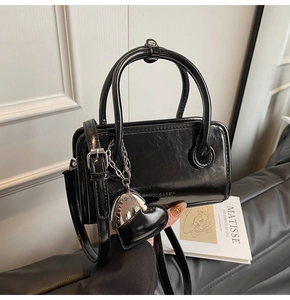 Detail of glossy black handbag with silver heart pendant and adjustable strap