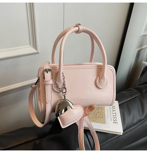 Detail of pink crossbody bag with heart charm and silver metal logo on artistic background